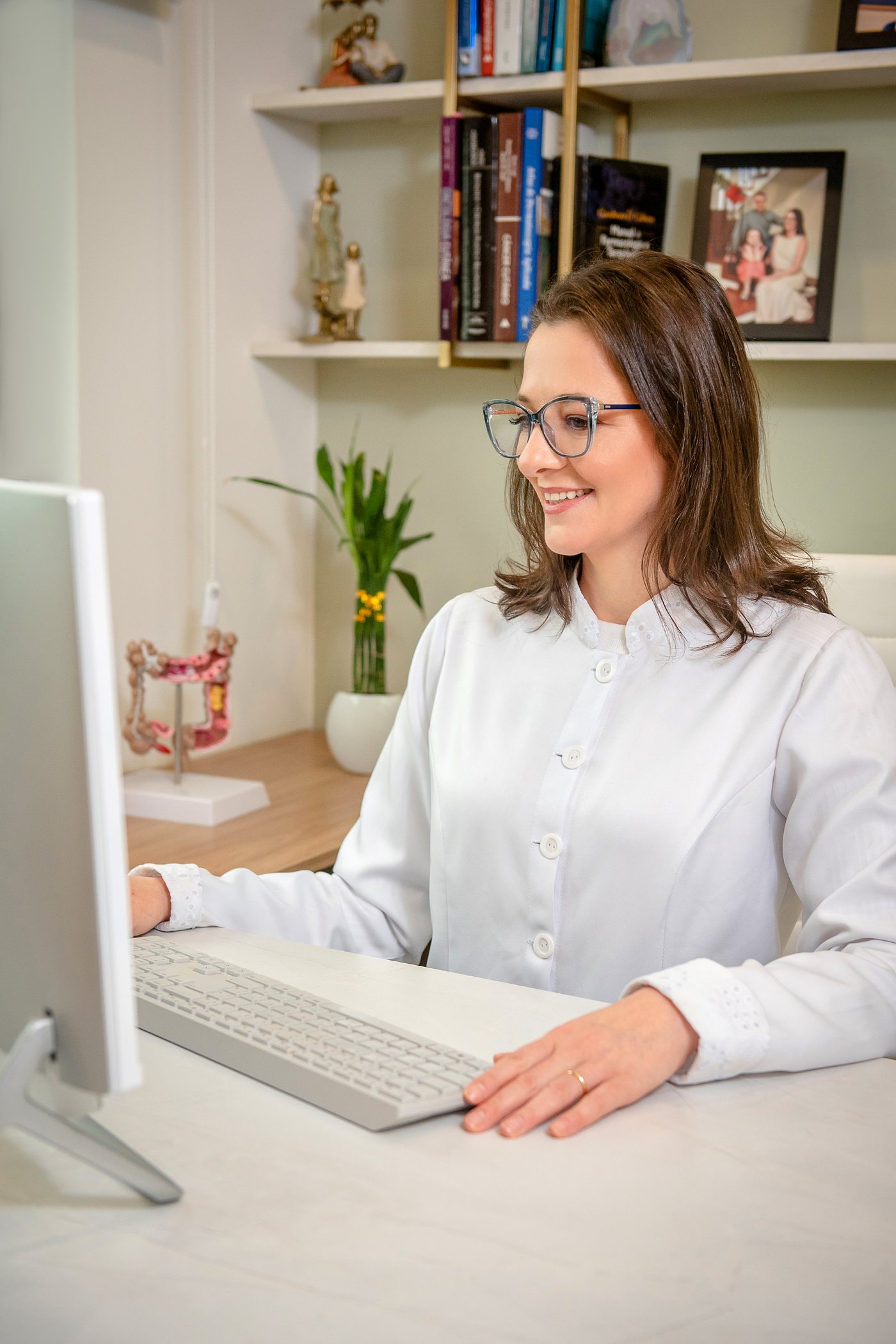 Dra. Luiza Fucilini analisando exames no monitor do consultório, com modelo anatômico ao lado